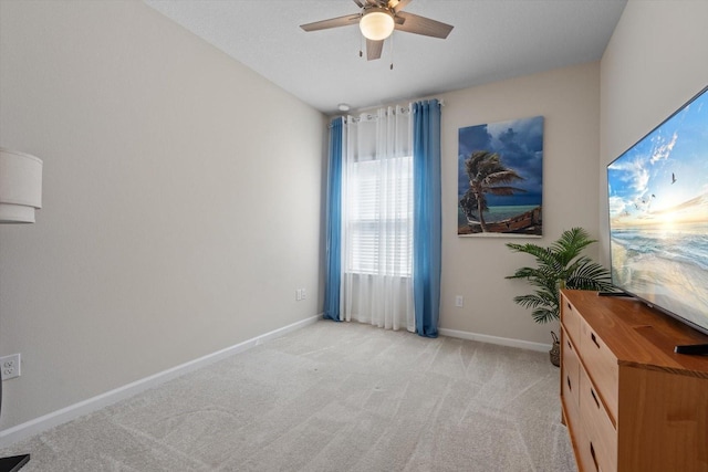 interior space with baseboards, a ceiling fan, and light colored carpet