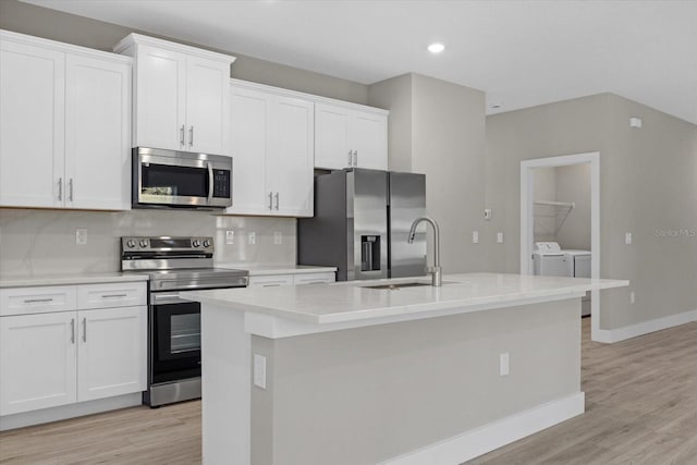 kitchen with appliances with stainless steel finishes, washer and clothes dryer, and an island with sink