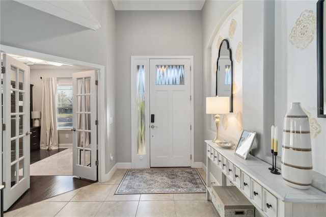 foyer entrance with light tile patterned floors, baseboards, ornamental molding, and french doors