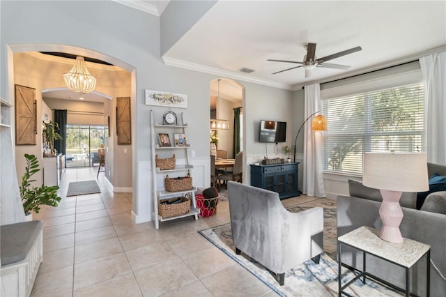 living area with baseboards, arched walkways, light tile patterned flooring, crown molding, and ceiling fan with notable chandelier