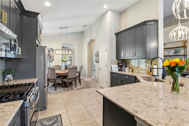 kitchen with arched walkways, stainless steel appliances, a sink, vaulted ceiling, and light stone countertops