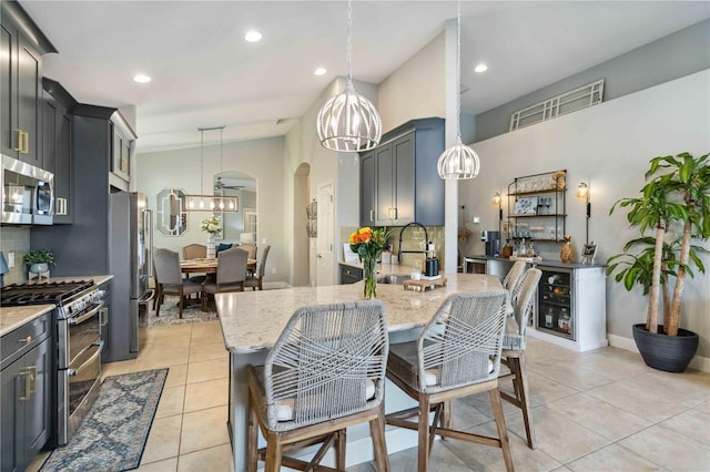 kitchen featuring arched walkways, light tile patterned floors, light stone counters, a sink, and appliances with stainless steel finishes