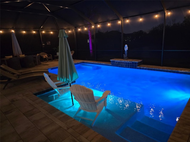 pool at night with an outdoor pool, glass enclosure, and a patio