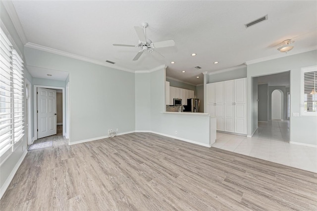 unfurnished living room with light wood finished floors, baseboards, visible vents, and arched walkways