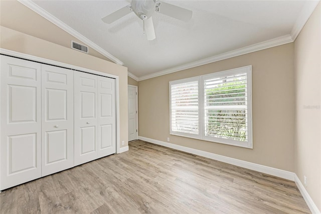 unfurnished bedroom featuring lofted ceiling, visible vents, ornamental molding, a closet, and light wood finished floors