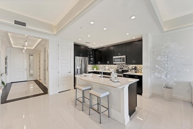 kitchen featuring a breakfast bar area, dark cabinets, a tray ceiling, stainless steel appliances, and light countertops