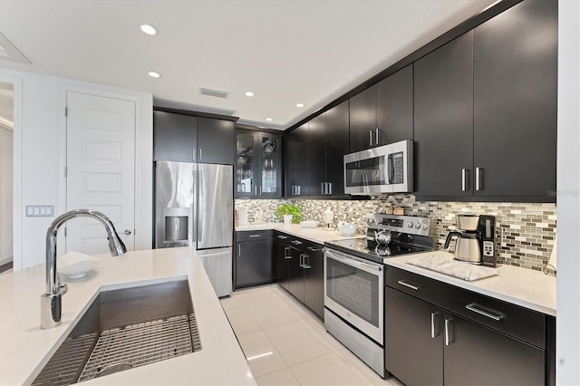 kitchen featuring a sink, appliances with stainless steel finishes, decorative backsplash, and dark cabinetry