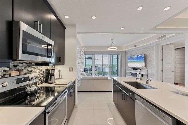 kitchen featuring dark cabinets, stainless steel appliances, a sink, open floor plan, and decorative backsplash