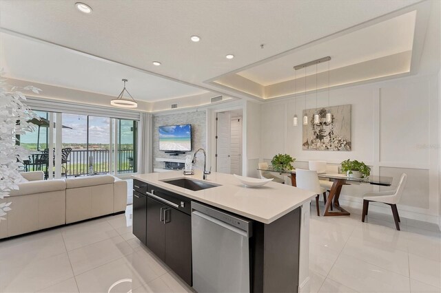 kitchen with a tray ceiling, hanging light fixtures, open floor plan, a sink, and dishwasher