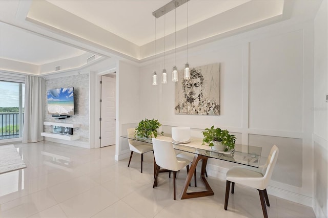 dining space with light tile patterned flooring, a raised ceiling, visible vents, and a decorative wall