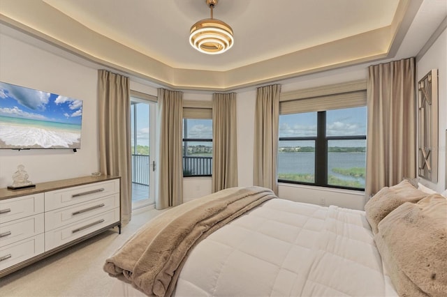 bedroom with access to exterior, a tray ceiling, light colored carpet, and a water view