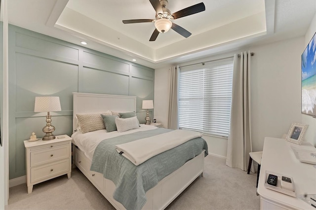 bedroom with light carpet, ceiling fan, a raised ceiling, and a decorative wall