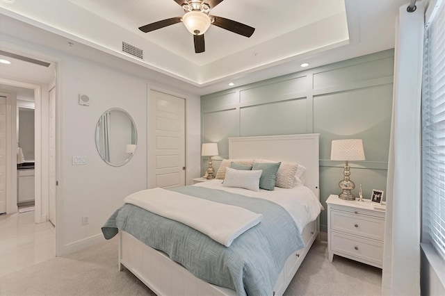 bedroom with light carpet, visible vents, a decorative wall, and a tray ceiling