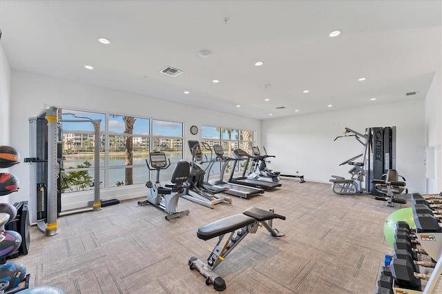 exercise room with a water view, carpet, visible vents, and recessed lighting