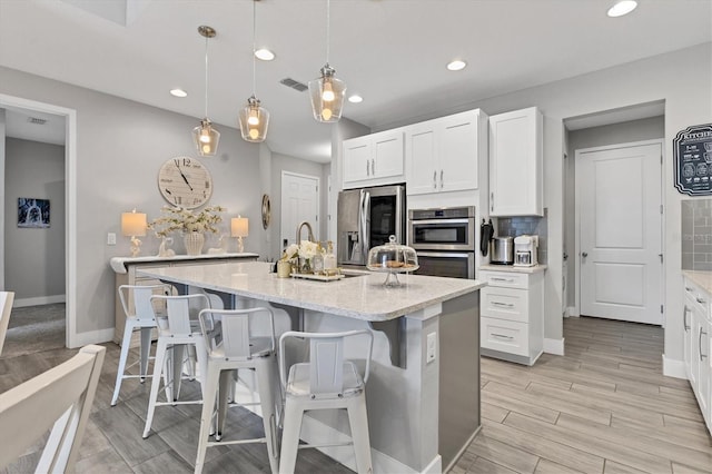 kitchen featuring visible vents, appliances with stainless steel finishes, hanging light fixtures, a kitchen island with sink, and white cabinetry