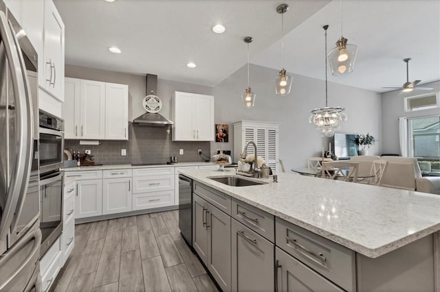 kitchen featuring a center island with sink, white cabinets, wall chimney exhaust hood, open floor plan, and a sink