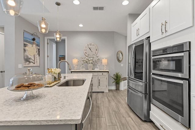 kitchen with visible vents, an island with sink, appliances with stainless steel finishes, white cabinetry, and a sink