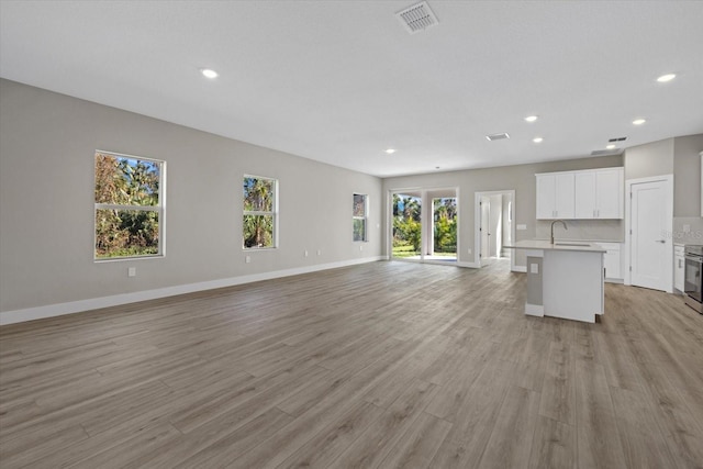 unfurnished living room with light wood finished floors, recessed lighting, visible vents, a sink, and baseboards