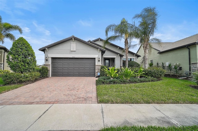 view of front of home with a garage, stone siding, decorative driveway, a front yard, and stucco siding