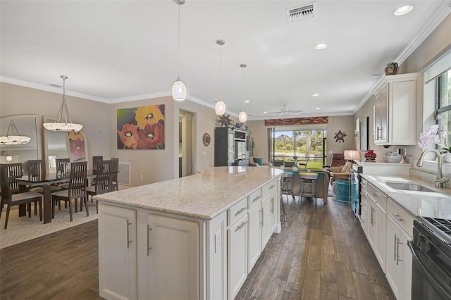 kitchen with a kitchen island, a sink, visible vents, white cabinetry, and hanging light fixtures