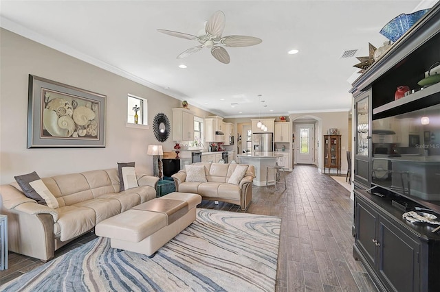 living area featuring crown molding, arched walkways, dark wood finished floors, and recessed lighting