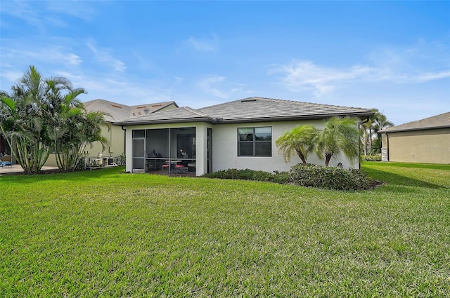 back of property with a sunroom, a tile roof, a yard, and stucco siding