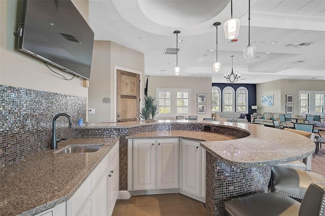 kitchen featuring a raised ceiling, hanging light fixtures, open floor plan, white cabinets, and a sink