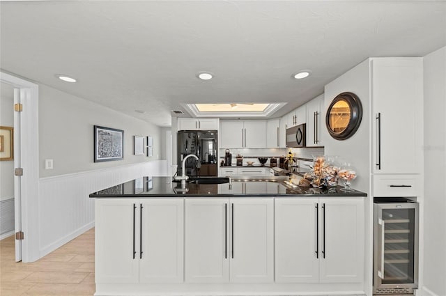 kitchen with a skylight, beverage cooler, black appliances, white cabinetry, and a sink