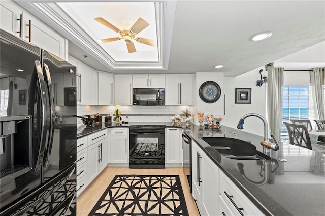 kitchen with a sink, white cabinetry, dark stone counters, black appliances, and a raised ceiling