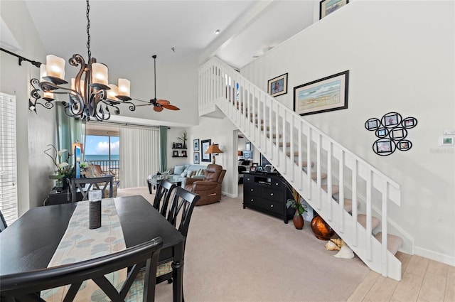 dining space with stairway, light carpet, high vaulted ceiling, baseboards, and ceiling fan with notable chandelier