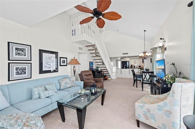 living area with high vaulted ceiling, light colored carpet, ceiling fan with notable chandelier, visible vents, and stairs