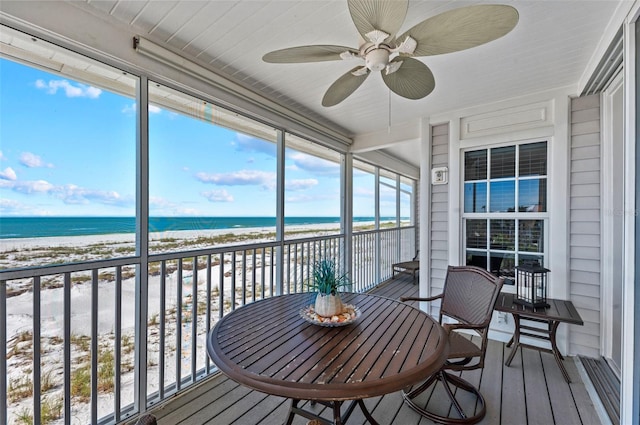 sunroom featuring ceiling fan, a water view, and a view of the beach