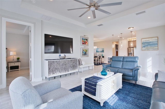 living area featuring a tray ceiling, wood finished floors, visible vents, and baseboards