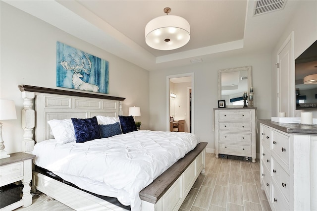 bedroom with a raised ceiling, visible vents, and connected bathroom