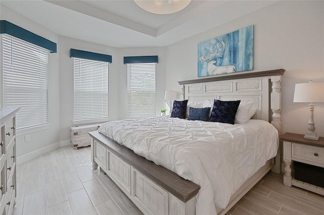 bedroom featuring wood tiled floor, a raised ceiling, and baseboards