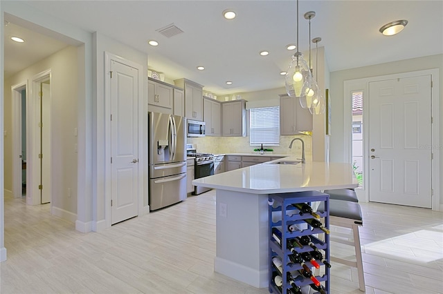 kitchen with a breakfast bar, stainless steel appliances, light countertops, pendant lighting, and a sink