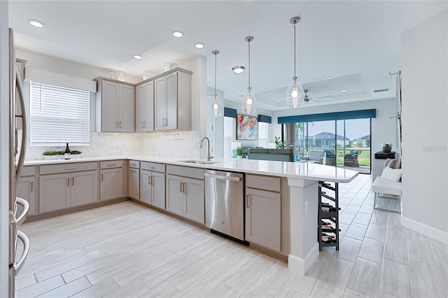 kitchen with appliances with stainless steel finishes, open floor plan, a peninsula, light countertops, and a sink