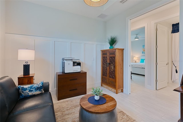 living area featuring wainscoting, a decorative wall, visible vents, and light wood finished floors