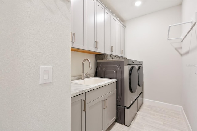 washroom with washing machine and dryer, cabinet space, a sink, and baseboards