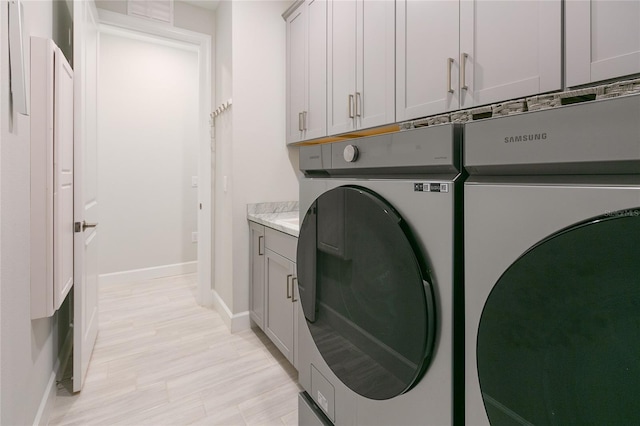 clothes washing area featuring cabinet space, washer and clothes dryer, and baseboards