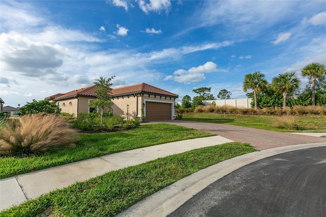 mediterranean / spanish home featuring a garage, a tiled roof, decorative driveway, stucco siding, and a front yard