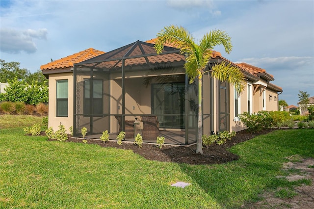 rear view of property featuring glass enclosure, a tile roof, a lawn, and stucco siding