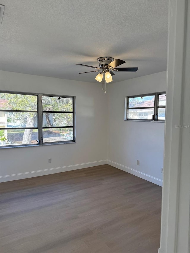 empty room featuring a textured ceiling, ceiling fan, dark wood-type flooring, and baseboards