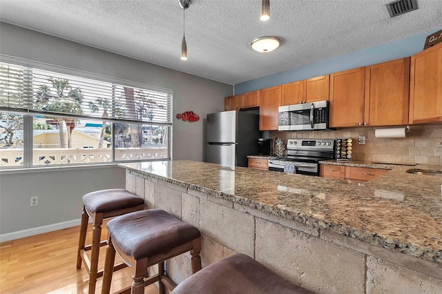 kitchen with light stone counters, visible vents, light wood-style floors, appliances with stainless steel finishes, and backsplash