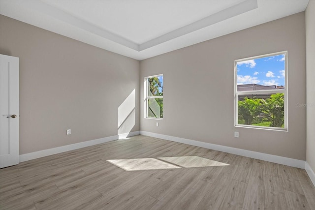 unfurnished room with light wood finished floors, baseboards, and a raised ceiling