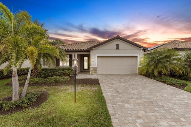 view of front facade featuring a garage, stone siding, a tiled roof, decorative driveway, and stucco siding