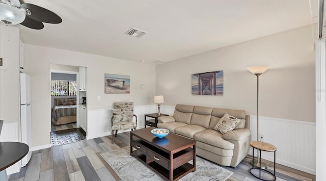 living area featuring a wainscoted wall, a ceiling fan, visible vents, and wood finished floors