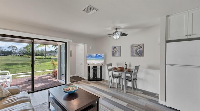 living area featuring ceiling fan, light wood-type flooring, visible vents, and baseboards