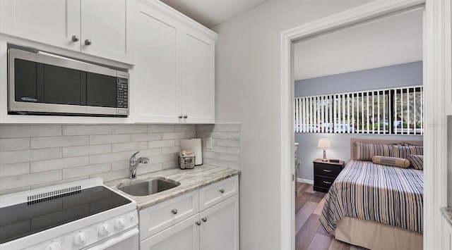 kitchen with a sink, white cabinets, electric stove, backsplash, and stainless steel microwave