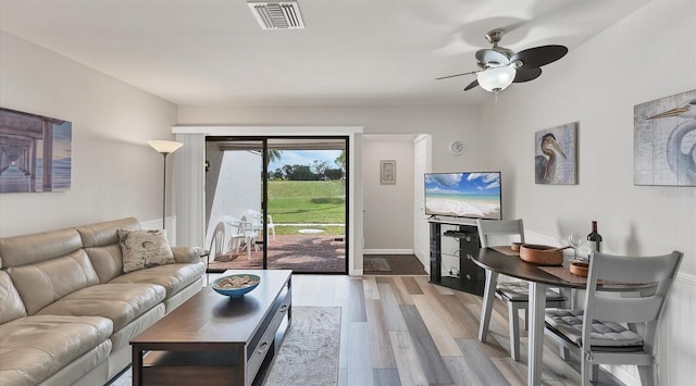 living area featuring baseboards, light wood finished floors, visible vents, and a ceiling fan